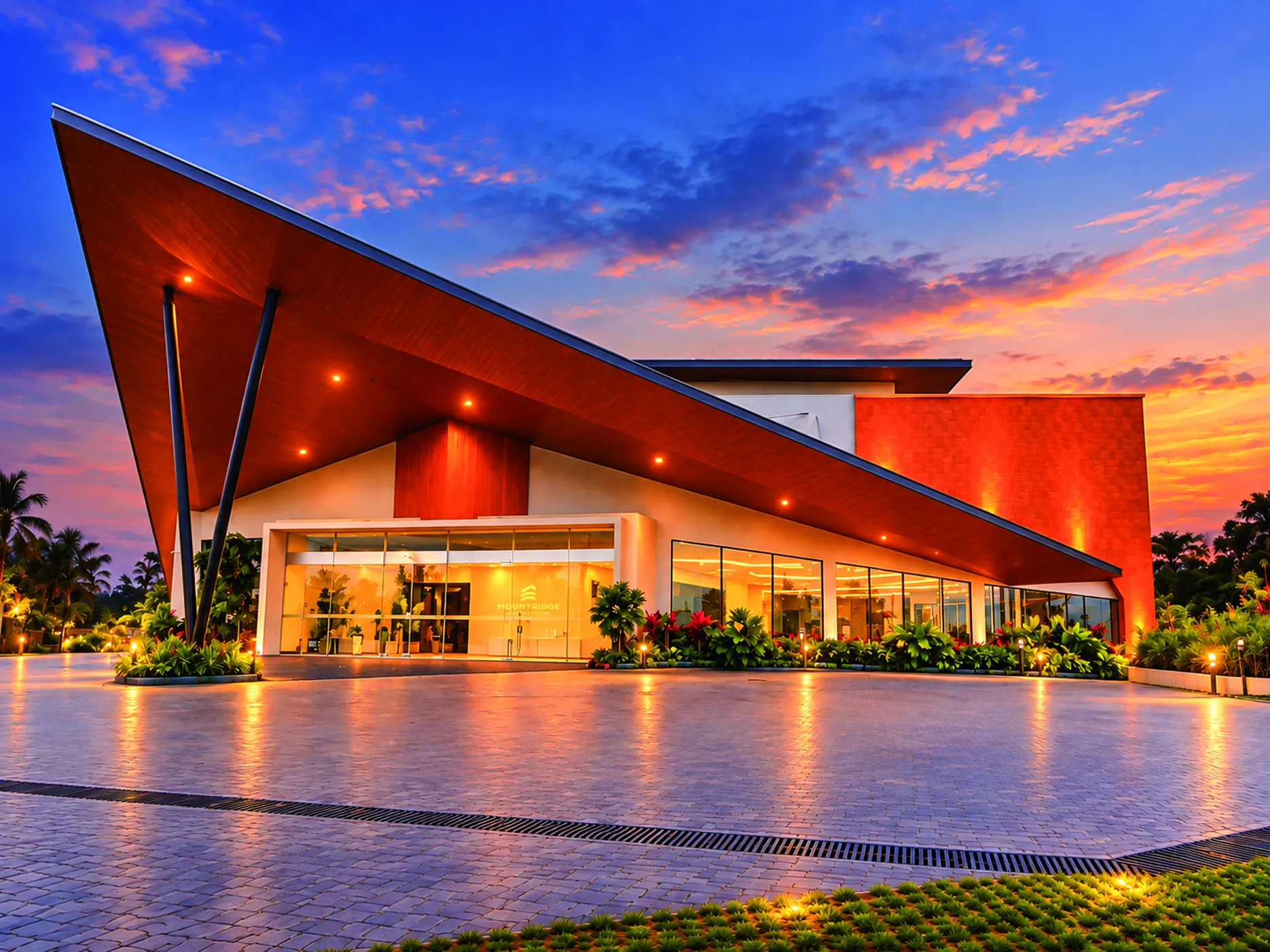 Mountridge International Convention Centre in Manjeri, Kerala at dusk, its cantilevered timber canopy lit above the glass entrance